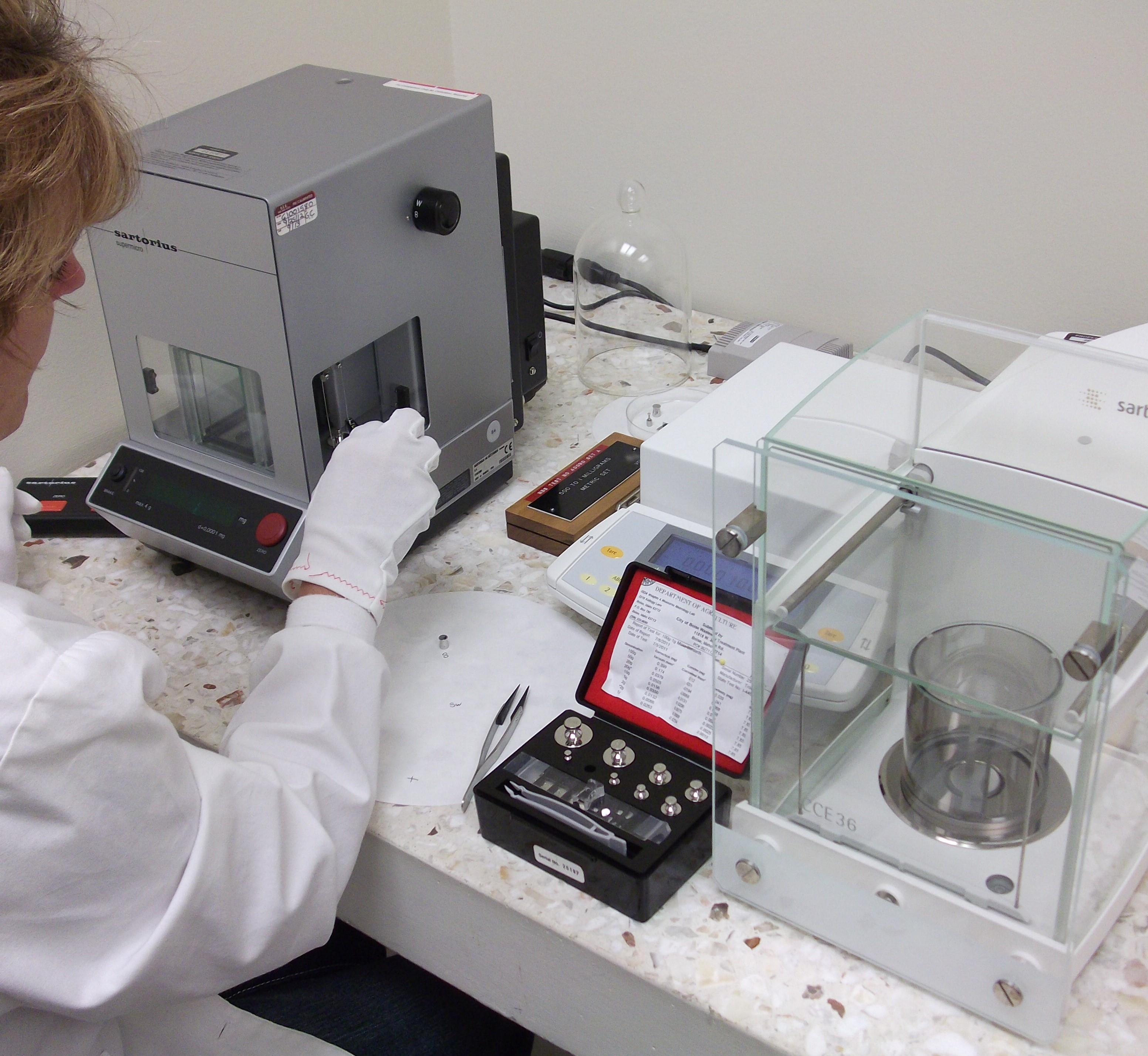 Employee in a laboratory with white gloves calibrating weights that are used to license weighing and measuring devices.