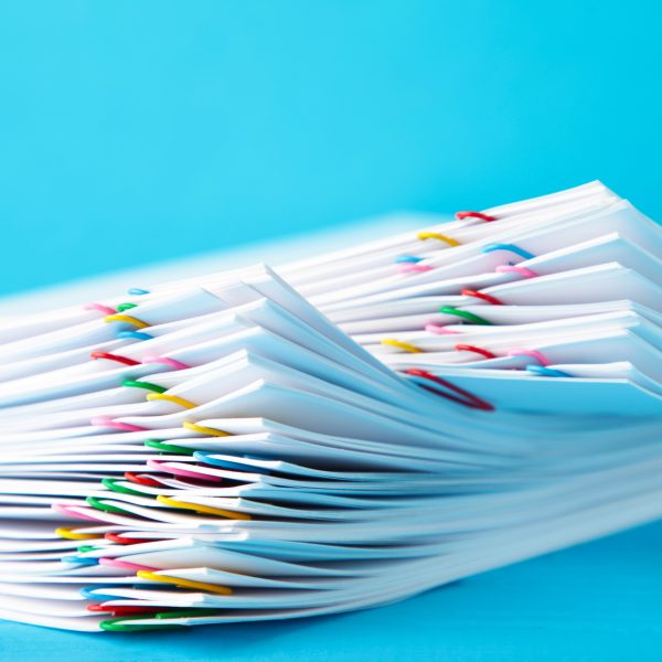 Side view of a stack of white papers with colorful paperclips against a blue background.
