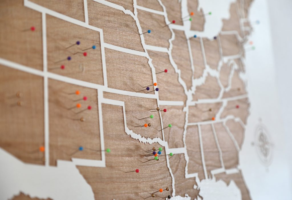 A view of a wooden map of the united states with pins in various parts of different states.