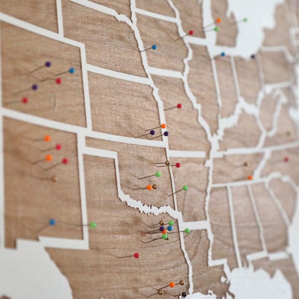 A view of a wooden map of the united states with pins in various parts of different states.